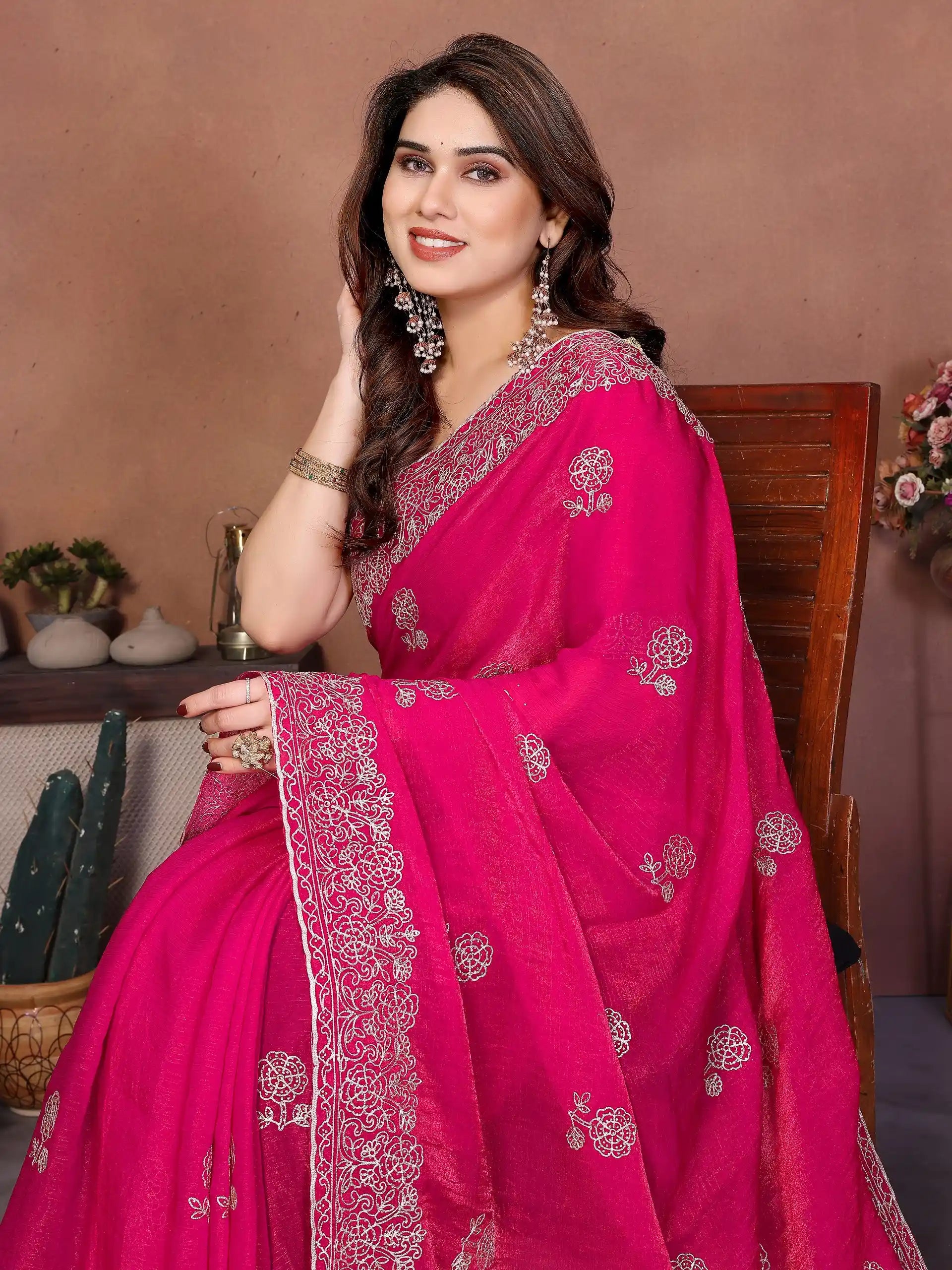 Woman wearing a bright pink saree with silver embroidery in an indoor setting.